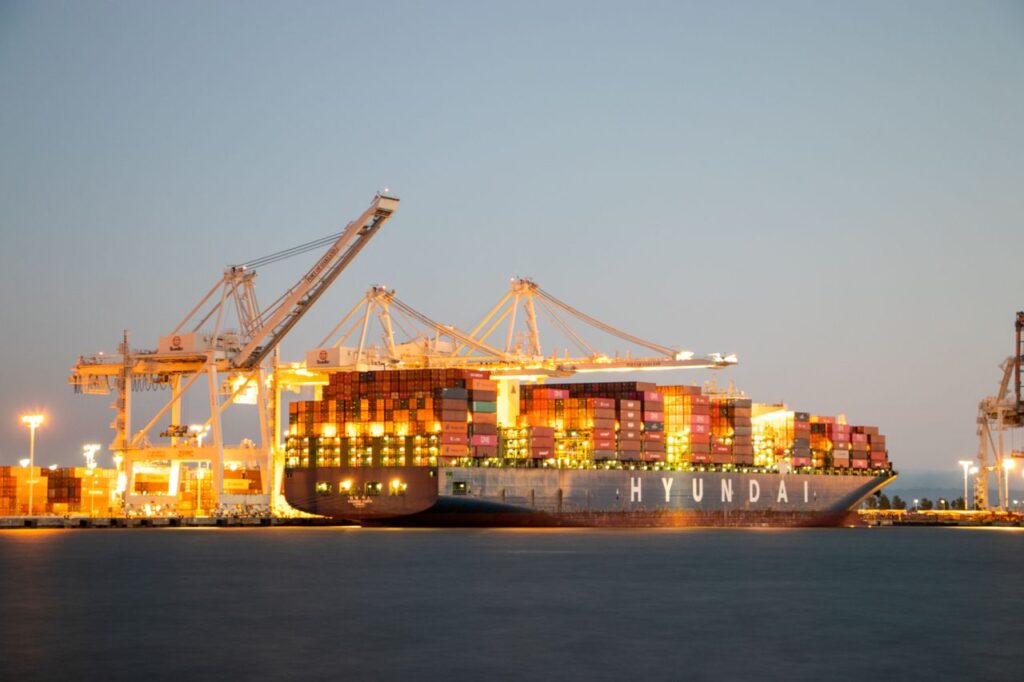 Mastering the First Impression: Your intriguing post title goes here Container ship docked at port under cranes during twilight, illuminated against the evening sky.
